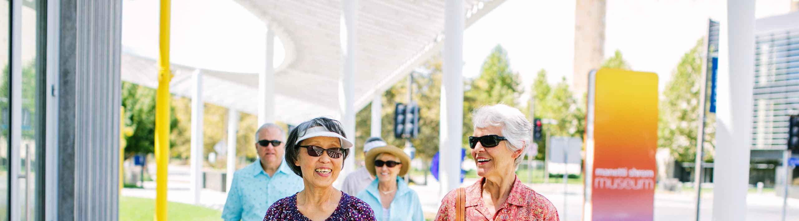 Smiling senior women wearing sunglasses walk in front of a museum